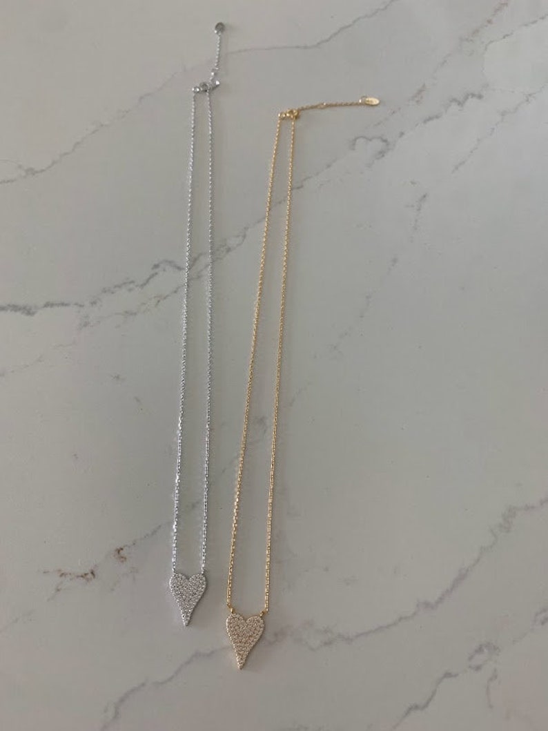 Puede incluir: Dos collares de plata y oro con un colgante de coraz&oacute;n. Cada coraz&oacute;n est&aacute; cubierto de peque&ntilde;as piedras transparentes.