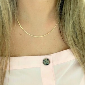 Könnte beinhalten: Eine goldene Kettenkette an einer Person, die ein rosa Hemd mit zwei Knöpfen trägt.