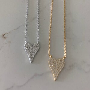 Puede incluir: Dos delicados collares con colgantes en forma de coraz&oacute;n. El colgante del collar de la izquierda es plateado y el colgante del collar de la derecha es dorado. Ambos colgantes est&aacute;n cubiertos de peque&ntilde;as piedras brillantes.