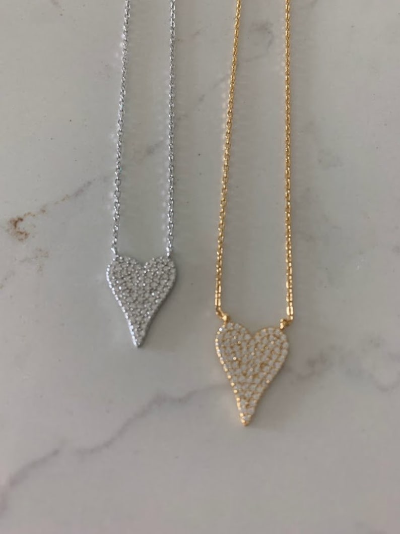 Puede incluir: Dos delicados collares con colgantes en forma de coraz&oacute;n. El colgante del collar de la izquierda es plateado y el colgante del collar de la derecha es dorado. Ambos colgantes est&aacute;n cubiertos de peque&ntilde;as piedras brillantes.