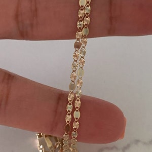 May include: A gold chain necklace with a delicate, patterned design. The chain is made of small, oval-shaped links with a textured surface.