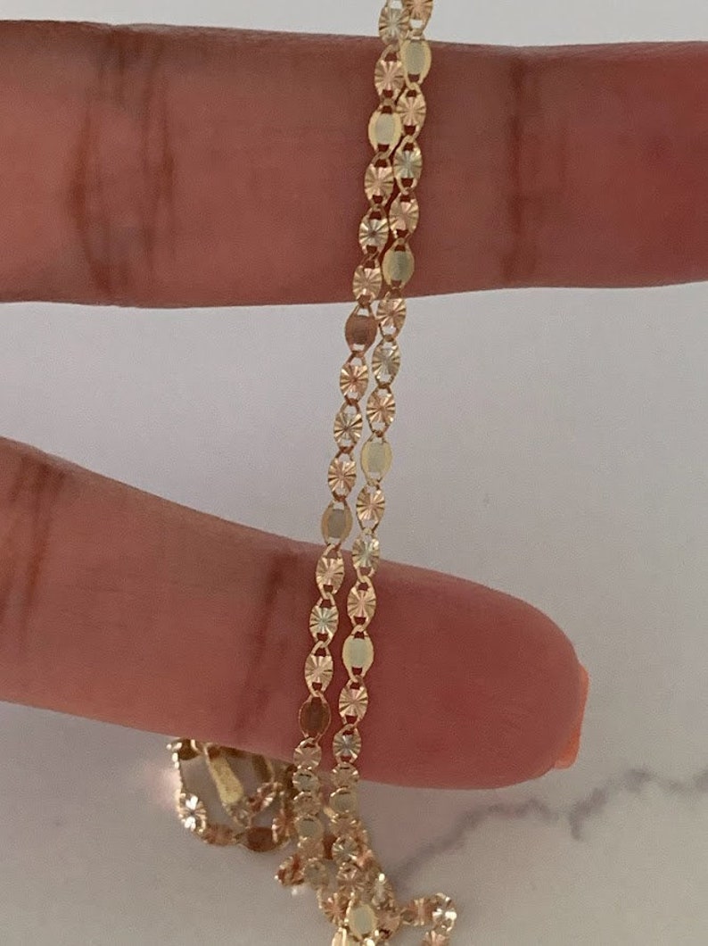 May include: A gold chain necklace with a delicate, patterned design. The chain is made of small, oval-shaped links with a textured surface.