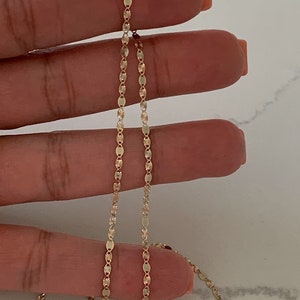 May include: A gold chain necklace with a delicate, patterned design. The chain is made of small, oval-shaped links.