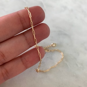 May include: A gold chain bracelet with a delicate, box chain design. The bracelet is made of a thin, gold chain and is approximately 7 inches in length.