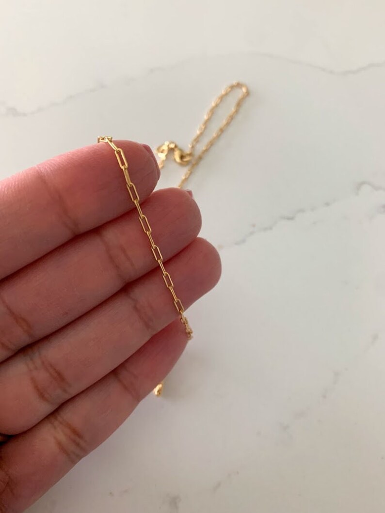 May include: A gold chain necklace with a delicate, box chain design. The chain is thin and has a subtle shine.