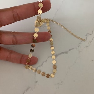 May include: A gold chain necklace with small, round, gold discs. The necklace is delicate and dainty.