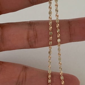 May include: A gold chain necklace with a delicate, patterned design. The chain is made of small, oval-shaped links.