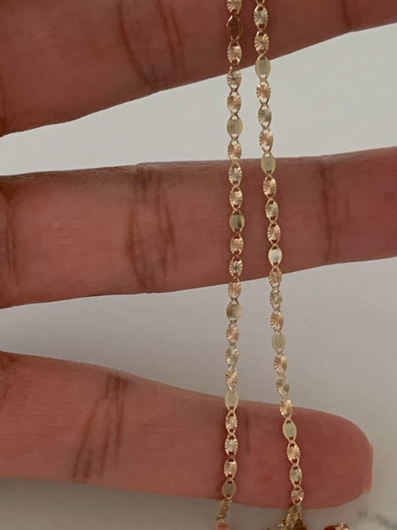 May include: A gold chain necklace with a delicate, patterned design. The chain is made of small, oval-shaped links.