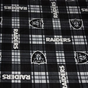 May include: Black and white plaid fabric with the repeated words "RAIDERS" and a black and white logo of a pirate skull with a sword.