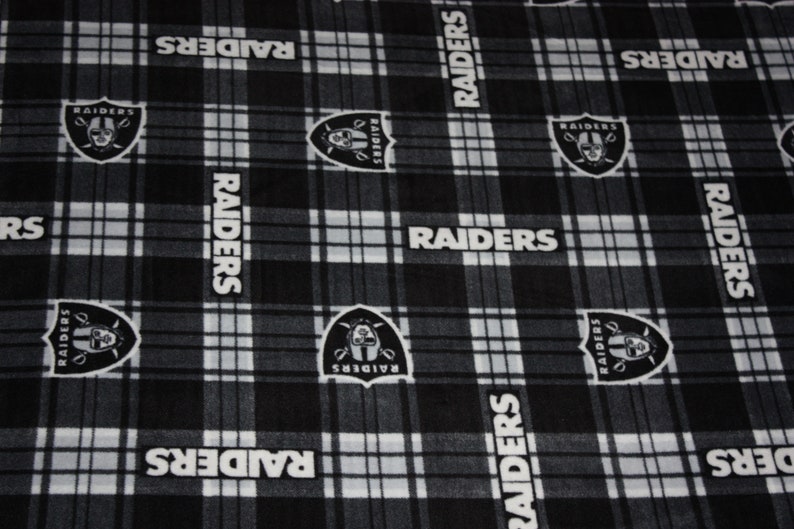 May include: Black and white plaid fabric with the repeated words "RAIDERS" and a black and white logo of a pirate skull with a sword.