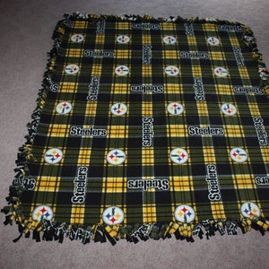 May include: A black and yellow plaid fleece blanket with the Pittsburgh Steelers logo and the word "Steelers" repeated throughout.