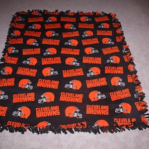 May include: A black and orange fleece blanket with the repeated text "Cleveland Browns" and a football helmet graphic.