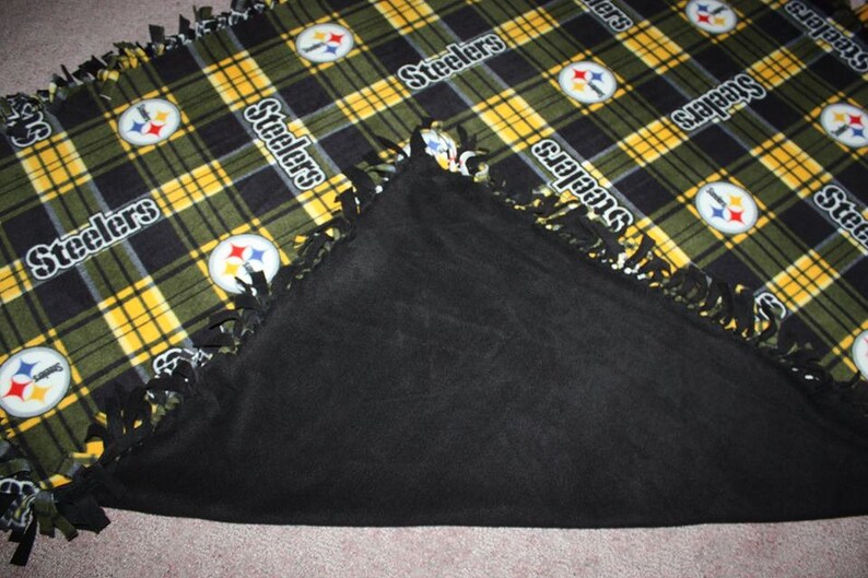 May include: A black and yellow fleece blanket with the Pittsburgh Steelers logo and the word "Steelers" repeated throughout. The blanket has a black fleece backing and a fringe border.