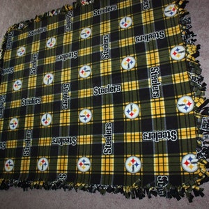 May include: A black and yellow plaid fleece blanket with the Pittsburgh Steelers logo repeated throughout. The blanket has a knotted fringe border.