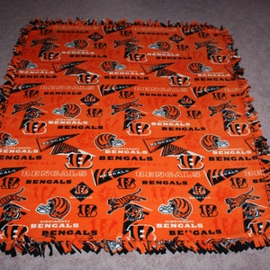 May include: An orange and black fleece blanket with a repeating pattern of the Cincinnati Bengals logo. The logo features a tiger head, the team name, and the number 16.
