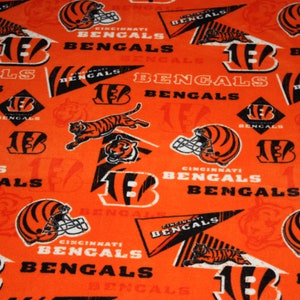 May include: Orange fabric with a repeating pattern of black and white Cincinnati Bengals logos, including the team's mascot, the number 13, and the words "Cincinnati Bengals".