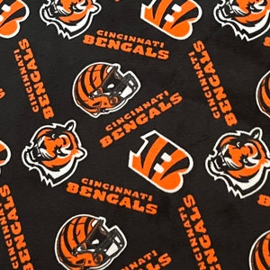 May include: Black fabric with a repeating pattern of orange and white Cincinnati Bengals logos. The logos include the team's mascot, a tiger, a football helmet, and the team's name.