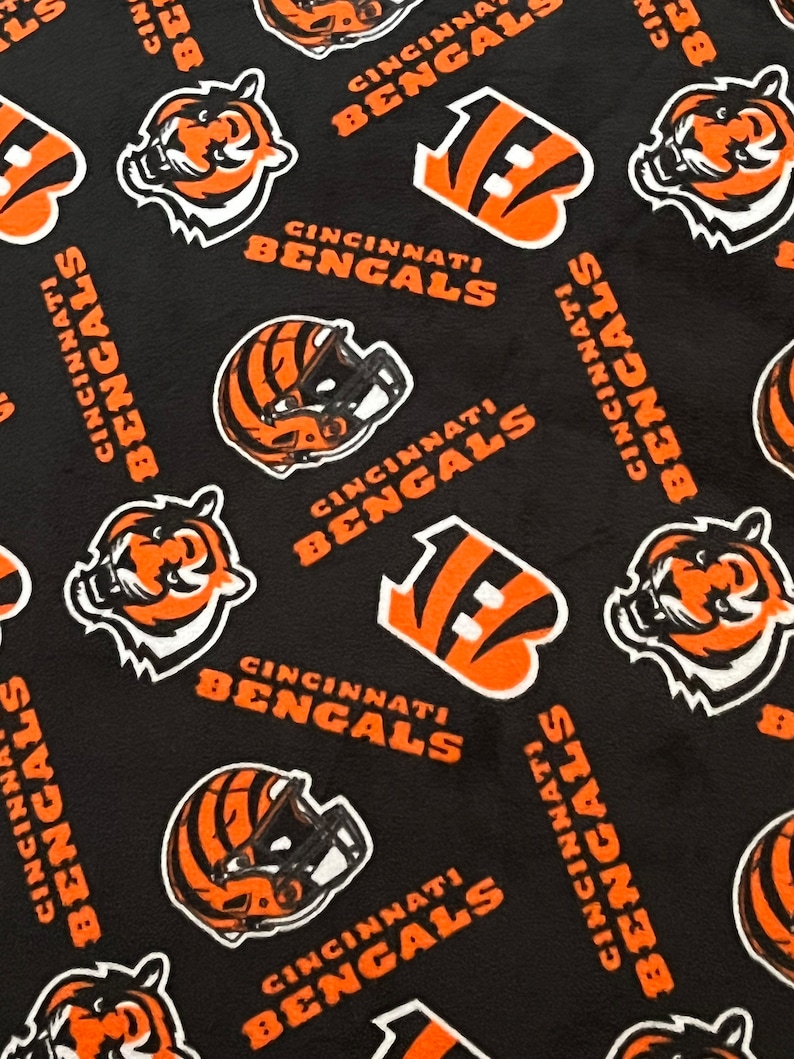 May include: Black fabric with a repeating pattern of orange and white Cincinnati Bengals logos. The logos include the team's mascot, a tiger, a football helmet, and the team's name.