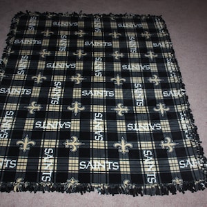 May include: A black and gold fleece blanket with a plaid pattern and the word "Saints" repeated throughout. The blanket has a frayed edge.