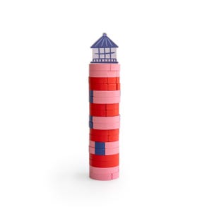 Könnte beinhalten: Ein Spielzeug-Leuchtturm aus gestapelten Blöcken in Rot-, Rosa- und Blautönen. Der Leuchtturm hat eine blau-weiße obere Struktur. Das Spielzeug steht vor einem weißen Hintergrund.