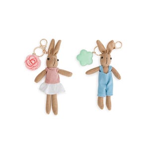 May include: Two plush bunny keychains. One bunny wears a pink and white outfit and has a pink rose charm. The other bunny wears blue overalls and has a green cloud charm. Both have gold-colored key rings.