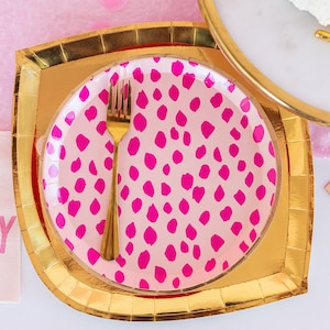 Op de afbeelding: Gouden en roze papieren feestborden met een roze stippenpatroon. Een gouden vork ligt op het bord.