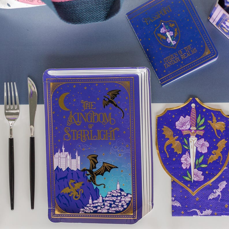 May include: A fantasy-themed party set featuring a book-shaped plate with the text "The Kingdom of Starlight", a passport, and a shield-shaped napkin. The set is decorated with dragons, castles, and floral accents in gold and purple.