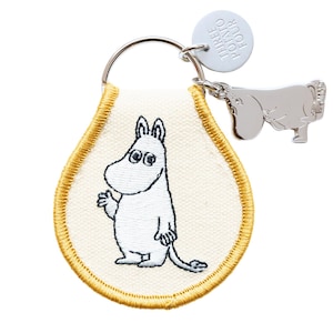 May include: Keyring featuring a white embroidered Moomin character on a cream-colored teardrop-shaped patch with gold stitching. A silver charm of a Moomin character and a round tag with the text "THREE POTATO FOUR" are attached to the keyring.