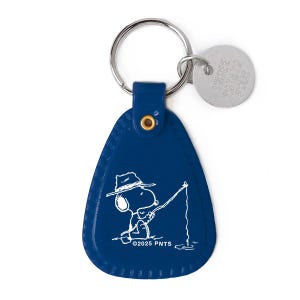 May include: A navy blue Snoopy keychain with a silver keyring and tag. The keychain features a white illustration of Snoopy fishing, wearing a hat. The text "©2025 PNTS" is below the illustration.