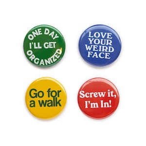 May include: Four round button badges with different sayings. The badges are green, blue, yellow, and red. The text on the badges reads: "One Day I'll Get Organized", "Love Your Weird Face", "Go for a Walk", and "Screw it, I'm In!"