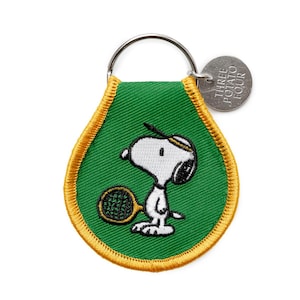 May include: Green Snoopy keychain with a gold border. The keychain features Snoopy playing tennis, holding a racket. A small silver tag reads "THREE POTATO FOUR". The keychain is attached to a silver key ring.