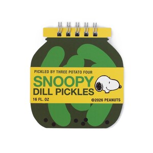 May include: A spiral-bound notepad shaped like a jar of pickles. The cover is dark green with a yellow label featuring the text PICKLED BY THREE POTATO FOUR SNOOPY DILL PICKLES 16 FL. OZ ©2026 PEANUTS and a graphic illustration of the character Snoopy.