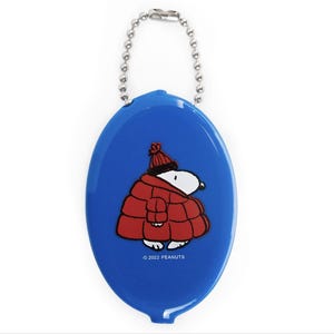 May include: Blue oval-shaped coin purse with a silver chain. The coin purse features a cartoon image of Snoopy wearing a red winter coat and hat. The text "© 2022 PEANUTS" is printed on the bottom of the coin purse.