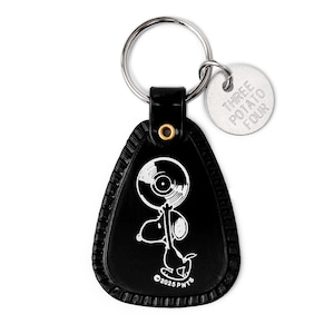 May include: Black leather keychain featuring a white illustration of Snoopy holding a vinyl record. The keychain has a silver ring and a small silver tag that reads "THREE POTATO FOUR". The bottom of the keychain reads "©2025 PNTS".