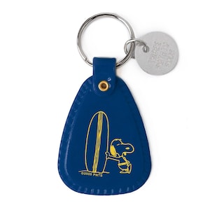 May include: A blue teardrop-shaped keychain featuring a yellow illustration of Snoopy with a surfboard. The keychain has a metal ring and a small, round metal tag. The text "©2025 PNTS" is printed on the keychain.