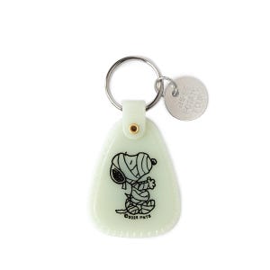 May include: A light green Snoopy keyring with a mummy design. The keyring has a metal ring and a small circular tag with the text "THESE POTATO FOUR". The Snoopy graphic is black and white. The keyring is made of plastic.