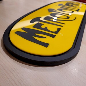K&ouml;nnte beinhalten: Ein gelbes ovales Schild mit schwarzem Rand und dem Text "METROPOLITAN" in schwarzen Buchstaben.