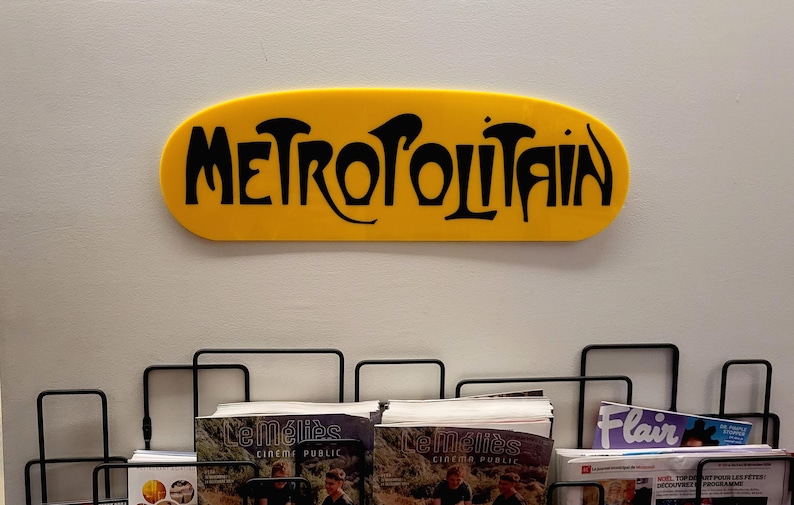 K&ouml;nnte beinhalten: Ein gelbes ovales Schild mit der Aufschrift "METROPOLITAIN" in schwarzen Buchstaben.