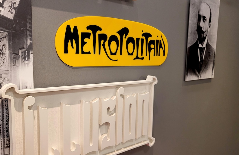 K&ouml;nnte beinhalten: Ein gelbes ovales Schild mit dem Wort "METROPOLITAIN" in schwarzen Buchstaben. Unter dem Schild befindet sich ein wei&szlig;es Schild mit dem Wort "USINE" in erhabenen Buchstaben.