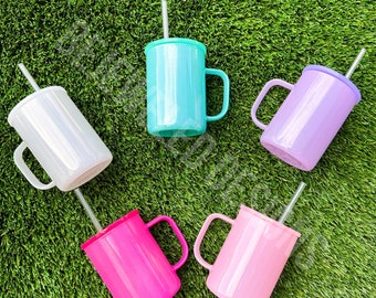 Puede incluir: Seis vasos de acero inoxidable con tapas y pajitas. Los vasos son de varios colores: blanco, azul claro, lavanda, rosa y rosa intenso. Los vasos están dispuestos en círculo sobre una superficie de hierba verde.