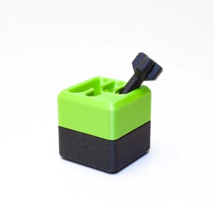 May include: A small, black and green 3D printed box with a black screw sticking out of the top.