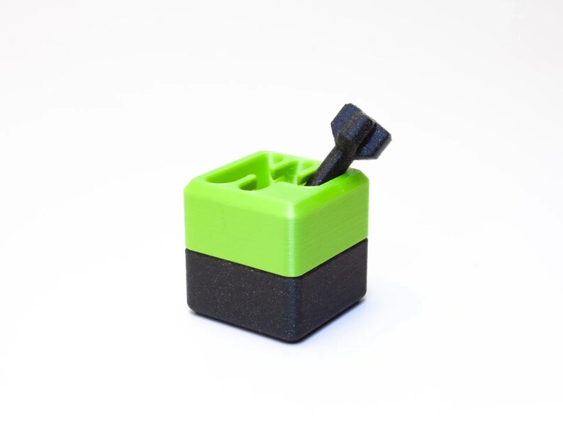 May include: A small, black and green 3D printed box with a black screw sticking out of the top.