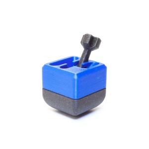 May include: A blue and black 3D printed puzzle cube with a black peg sticking out of the top.