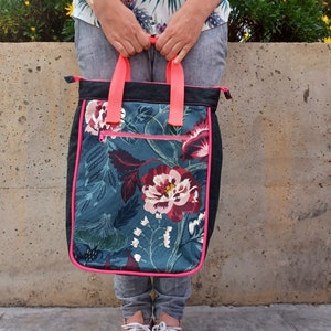 May include: A black tote bag with a floral print and pink trim. The bag has a zipper closure and two pink handles.