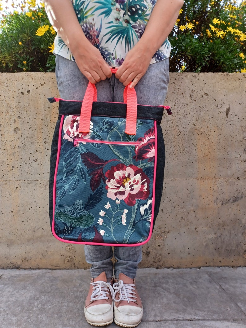 May include: A black tote bag with a floral print and pink trim. The bag has a zipper closure and two pink handles.