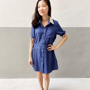 May include: A blue collared dress with white lace trim on the collar and cuffs. The dress has a button-up front and a belt.