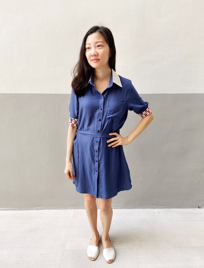 May include: A blue collared dress with white lace trim on the collar and cuffs. The dress has a button-up front and a belt.