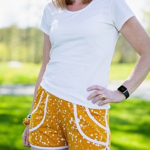 May include: A woman wearing a white t-shirt and yellow shorts with white polka dots. The shorts have white piping and a white pocket on the side.