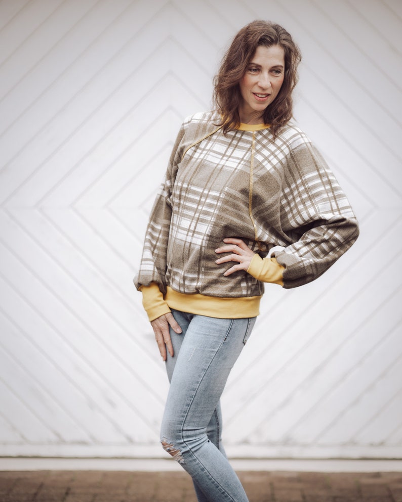 Pode incluir: Uma mulher vestindo uma camisa marrom e branca xadrez com uma borda amarela e jeans azul.