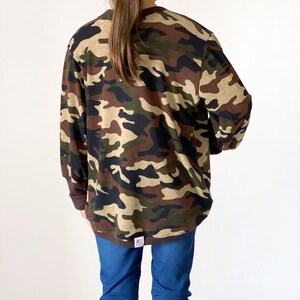 May include: A long-sleeved shirt with a camouflage pattern in shades of brown, green, and beige. The shirt has a crew neck and is made of a soft, comfortable fabric.